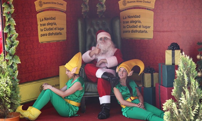 Santa sitting on a chair with two elves sitting on the floor in front of him